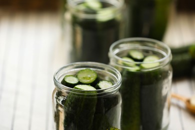 Photo of Glass jars with fresh cucumbers prepared for canning against blurred background, closeup