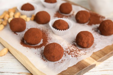 Delicious chocolate truffles powdered with cocoa on wooden board, closeup