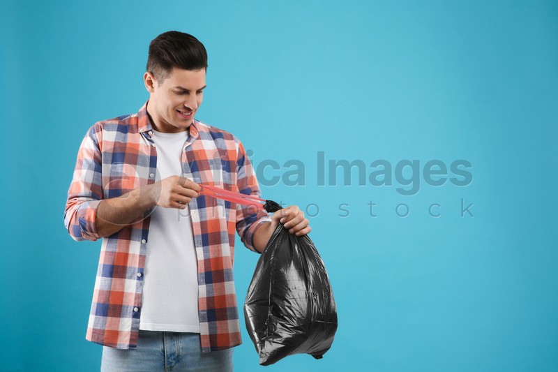 Man holding full garbage bag on light blue background. Space for text