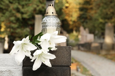 White lilies and grave light on grey granite tombstone outdoors, space for text. Funeral ceremony