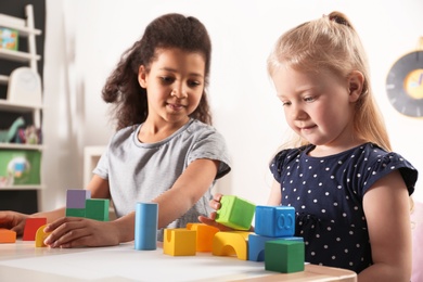 Cute little children playing with building blocks in kindergarten. Indoor activity