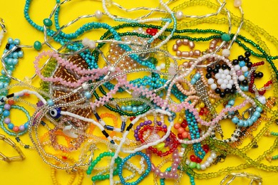 Pile of beautiful handmade beaded jewelry on yellow background, top view