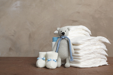 Photo of Baby diapers, toy bear and child's booties on wooden table. Space for text