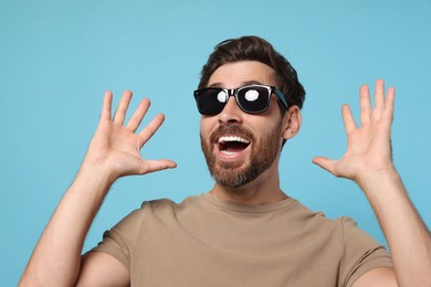 Portrait of excited bearded man with stylish sunglasses on light blue background