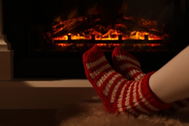 Woman in warm socks resting near fireplace with burning woods indoors, closeup
