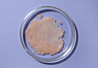 Petri dish with sample on lilac background, top view