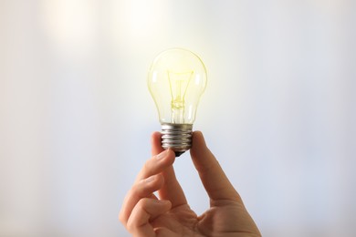 Woman holding light bulb on blurred background, closeup