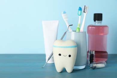 Tooth model, oral hygiene products and dentist tool on turquoise wooden table, space for text