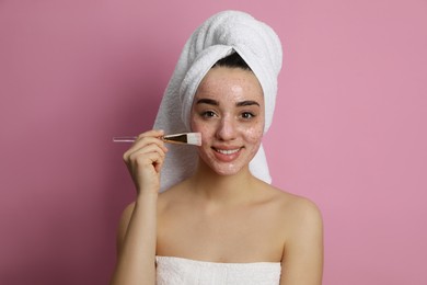 Woman applying pomegranate face mask on pink background