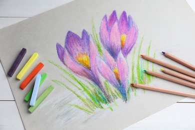 Colorful chalk pastels, pencils and beautiful painting of crocus flowers on white wooden table, above view