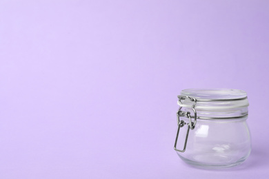 Closed empty glass jar on lilac background, space for text