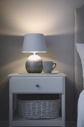 Photo of Stylish lamp and cup of drink on white nightstand in room