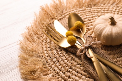 Photo of Autumn table setting. Cutlery with pumpkin and wicker mat on white wooden background, closeup