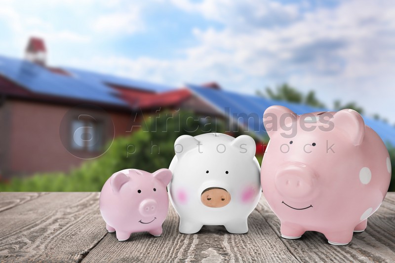 Piggy banks on wooden surface and blurred view of beautiful house. Mortgage concept