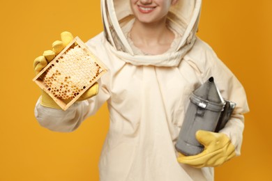 Photo of Beekeeper in uniform holding smokepot and hive frame with honeycomb on yellow background, closeup