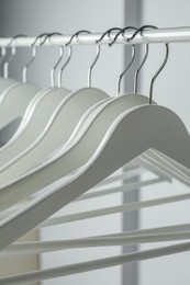 Photo of White clothes hangers on metal rail against light background, closeup