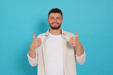 Young man showing thumbs up on light blue background