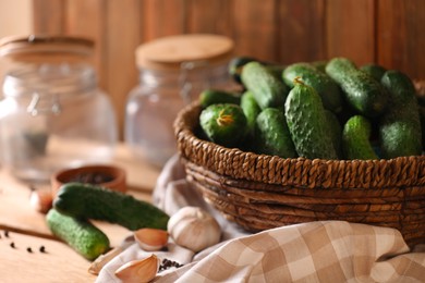 Photo of Fresh cucumbers and other ingredients near empty jars prepared for canning on wooden table, closeup
