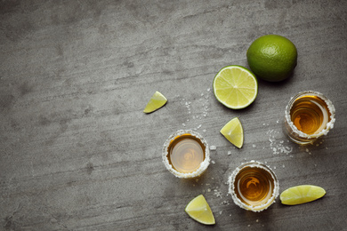 Mexican Tequila shots, lime slices and salt on grey table, flat lay. Space for text