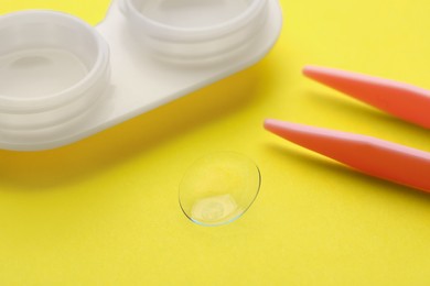 Photo of Contact lens, case and tweezers on yellow background, closeup
