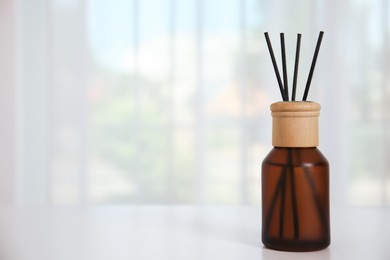 Reed diffuser on white table against window in room. Space for text