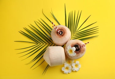 Fresh coconuts with drinking straws and flowers on yellow background, flat lay