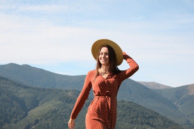 Young woman with straw hat walking in beautiful mountains on sunny day