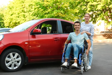 Young woman with disabled man in wheelchair near car outdoors