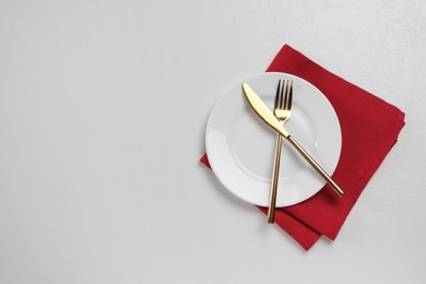 Photo of Clean plate and golden cutlery on white table, flat lay. Space for text