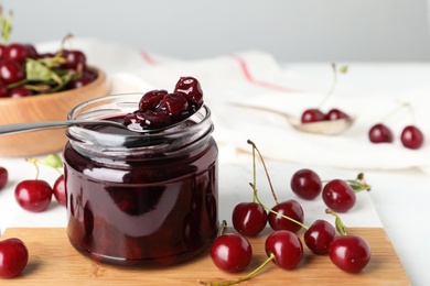Jar of pickled cherries and fresh fruits on table, closeup