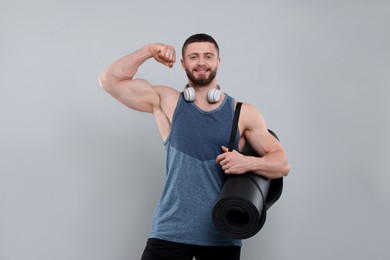 Photo of Handsome man with fitness mat and headphones showing muscles on grey background, space for text