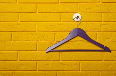 Empty clothes hanger on yellow brick wall, space for text