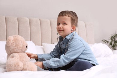 Cute little boy playing with stethoscope and toy bear in bedroom. Future pediatrician