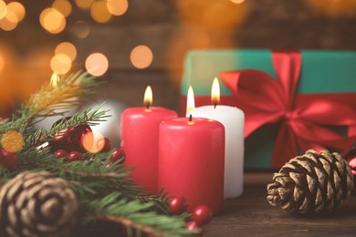 Burning candles, gift box and festive decor on wooden table, bokeh effect. Christmas eve