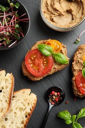 Slices of bread with delicious pate, tomatoes and basil on black table, flat lay