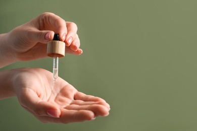 Photo of Woman dripping serum from pipette on her hand against olive background, closeup. Space for text