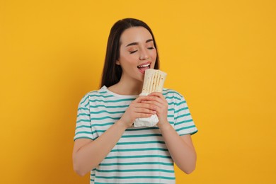 Photo of Young woman eating tasty shawarma on yellow background