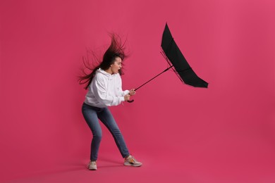 Emotional woman with umbrella caught in gust of wind on pink background