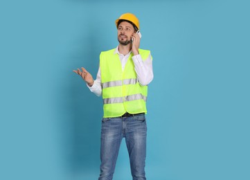 Photo of Male industrial engineer in uniform talking on phone against light blue background