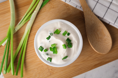 Fresh sour cream with onion on wooden board, top view