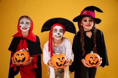 Cute little kids with pumpkin candy buckets wearing Halloween costumes on yellow background