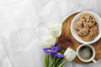 Delicious coffee, cookies and flowers on white cloth, flat lay. Space for text