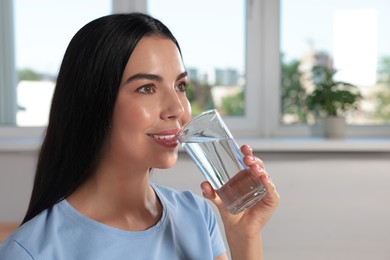 Young woman drinking water indoors, space for text. Refreshing drink