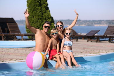 Happy family with inflatable ball at poolside on sunny summer day