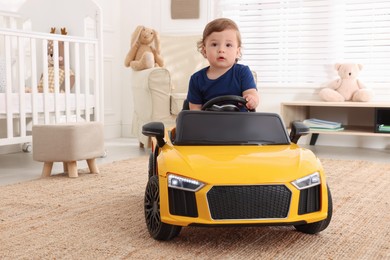 Adorable child driving yellow toy car in room