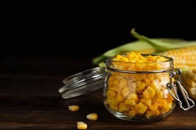 Tasty sweet corn kernels in jar on wooden table. Space for text