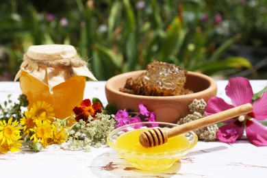 Delicious honey, combs and different flowers on white wooden table in garden