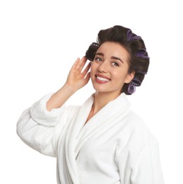Happy young woman in bathrobe with hair curlers on white background