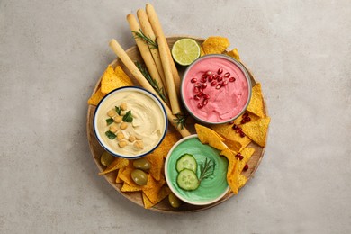 Different kinds of tasty hummus served with snacks on light table, top view