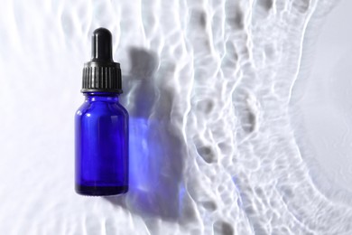 Bottle of face serum in water on white background, top view. Space for text